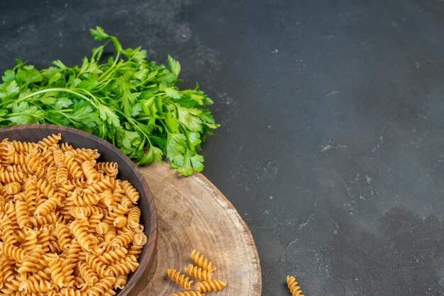 Above view of raw pastas inside and outside brown pot green bundle on the right side on dark blue color background