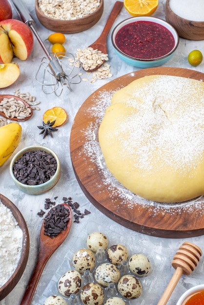 Above view of raw pastry on round board and set of various foods grater on ice background