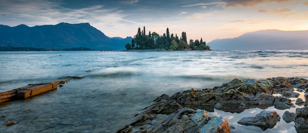 View of a sea with a small island full of tree in the middle with the mountains