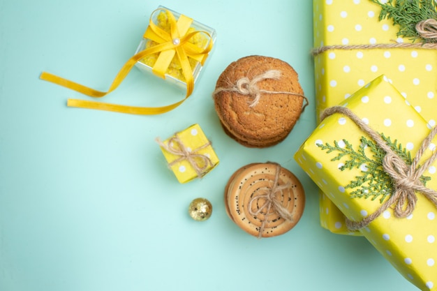 Above view of stacked various delicious cookies and beautiful yellow gift boxes next to decoration accessory on pastel green background