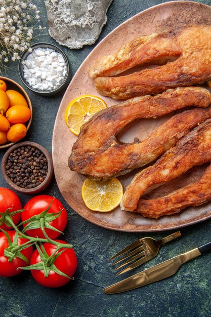 Above view of tasty fried fishes and lemon slices on a brown plate tomatoes kumquats on mix colors table with free space