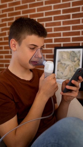 View of teenage boy using nebulizer at home for respiratory health problems