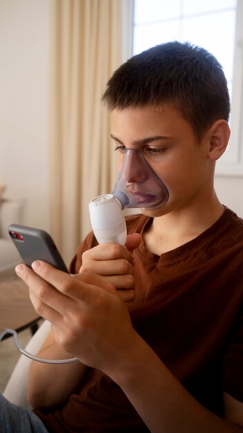 View of teenage boy using nebulizer at home for respiratory health problems