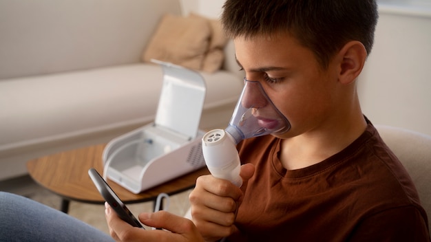 View of teenage boy using nebulizer at home for respiratory health problems