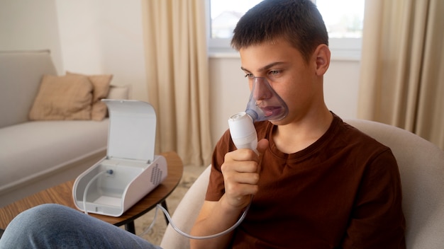 View of teenage boy using nebulizer at home for respiratory health problems