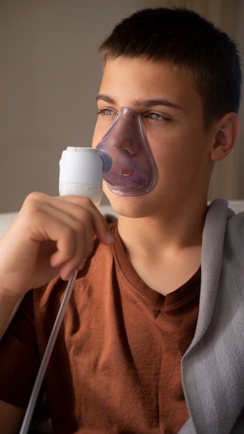 View of teenage boy using nebulizer at home for respiratory health problems