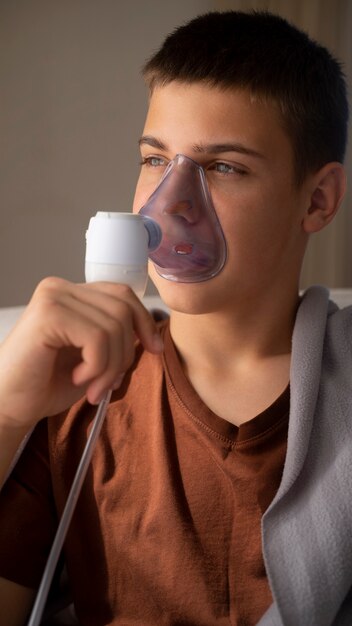 View of teenage boy using nebulizer at home for respiratory health problems