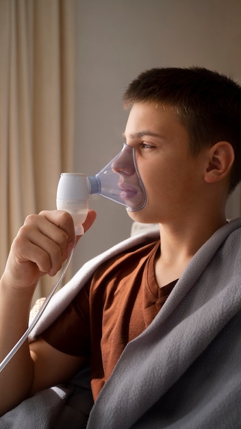 View of teenage boy using nebulizer at home for respiratory health problems