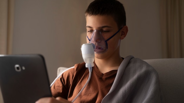 View of teenage boy using nebulizer at home for respiratory health problems