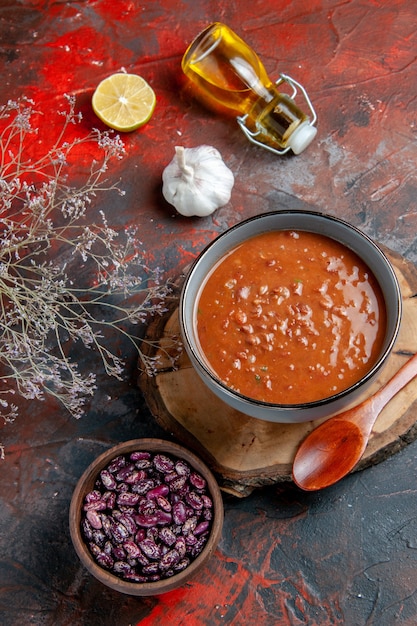 Free photo above view of tomato soup in a blue bowl on a tray beans oil bottle on mixed color table