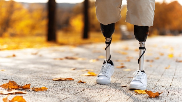 View of a walking man with prosthetic legs and white sneakers Fallen yellow leaves on the ground