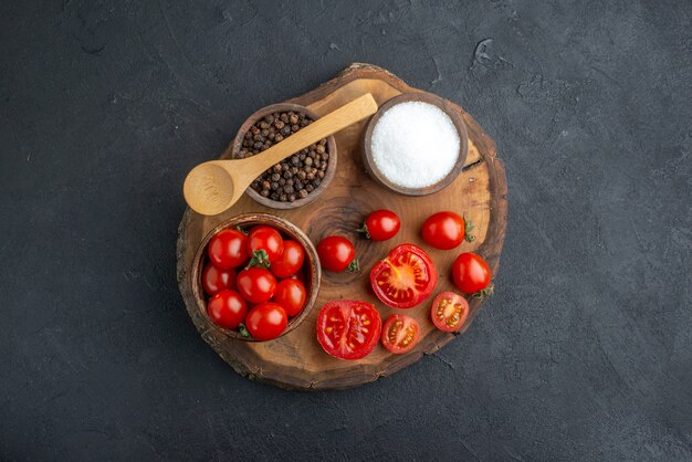 Above view of whole cut fresh tomatoes and pepper on wooden board on black surface with free space