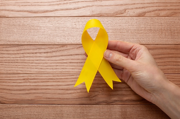 Free photo view of yellow ribbon with human hand on wooden background