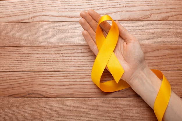 Free photo view of yellow ribbon with human hand on wooden background