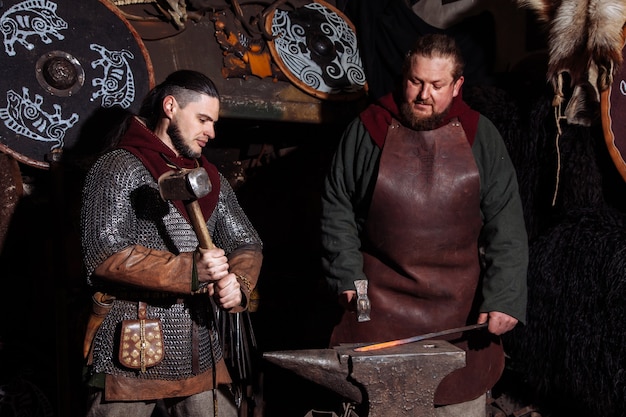 Viking forges weapons and swords in the smithy. A man in a warrior's clothes is in the smithy