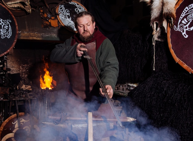 Viking forges weapons and swords in the smithy. A man in a warrior's clothes is in the smithy