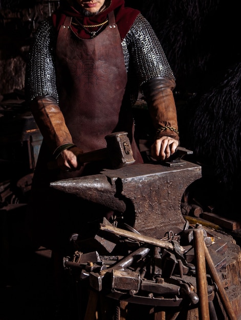 Viking forges weapons and swords in the smithy. A man in a warrior's clothes is in the smithy