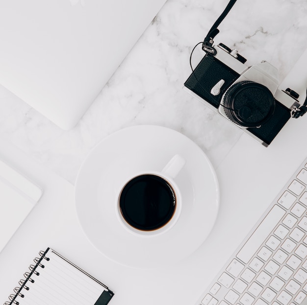 Vintage camera; keyboard; coffee cup and diary on white marble backdrop