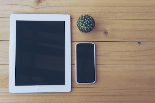 Vintage tone of top view of tablet and mobile on wooden table with small cactus