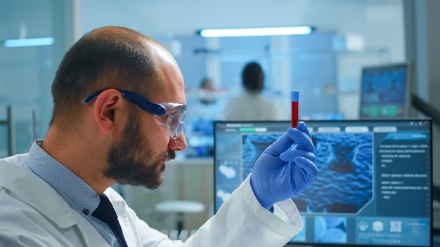 Free photo viorolog researcher examining blood sample from test tube working in modern equipped laboratory