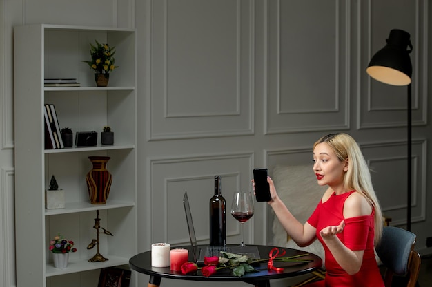 Free photo virtual love cute blonde girl in red dress on distance date with wine and candles talking on phone