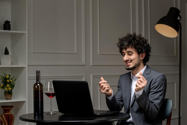 Virtual love handsome cute guy in suit with wine on a distance computer date showing finger hearts