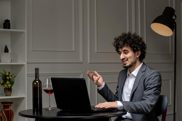 Virtual love handsome cute guy in suit with wine on a distance computer date talking on camera