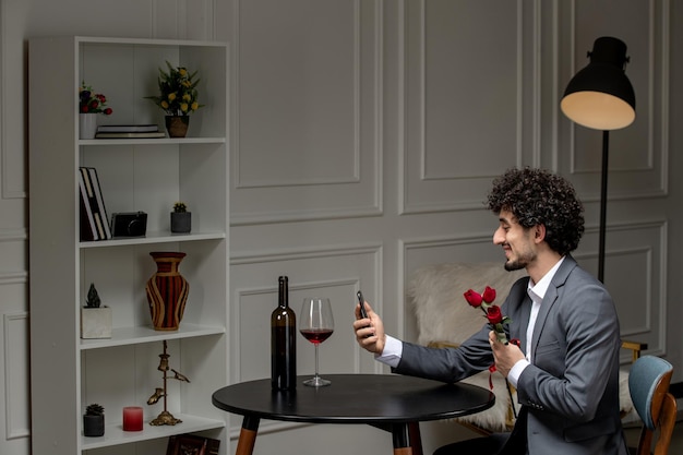 Virtual love handsome cute guy in suit with wine on a distance phone date holding flowers