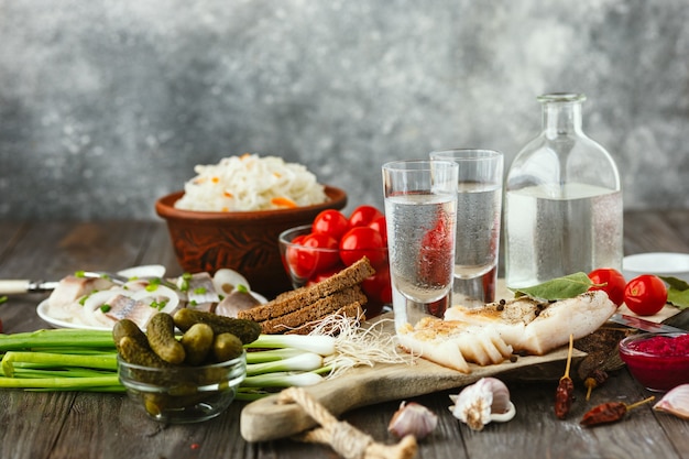 Vodka with lard, salted fish and vegetables on wooden table