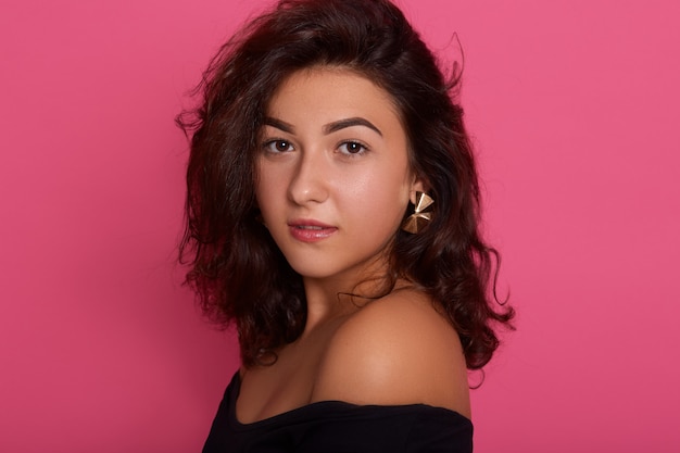 Vogue style close-up portrait of beautiful woman with curly hair posing isolated over pink wall,  with confident expression.