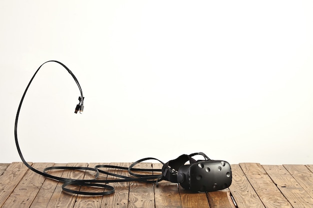 VR headset and some cords on rough rustic wooden table on white wall