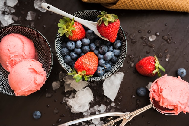 Waffle cone near fresh berries and ice cream on dishes and spoon among melted ice