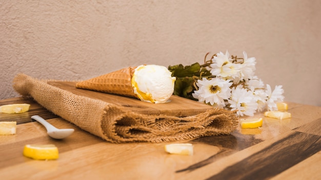 Waffle cone with ice cream near slices of fresh fruits and flowers on napkin