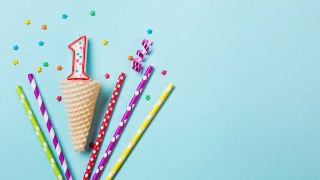 Free Photo waffle cone with number one candle; streamer and drinking straws on blue background