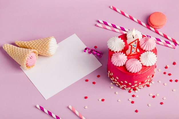 Waffle cones on paper near the delicious cake with sprinkles and drinking straws on purple backdrop