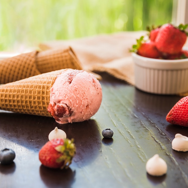 Waffle cones with ice cream near fresh berries in bowl and napkin on table