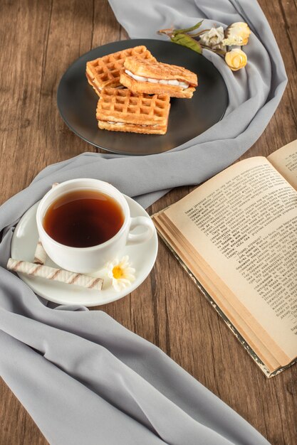 Waffles in a black saucer, a cup of tea and a book.