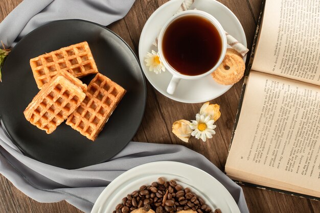 Waffles in a black saucer and a cup of tea. top view