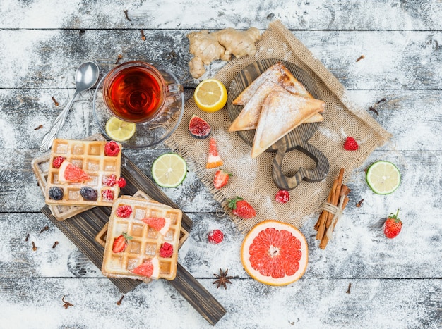 Waffles and teaon wooden board with berries and citrus