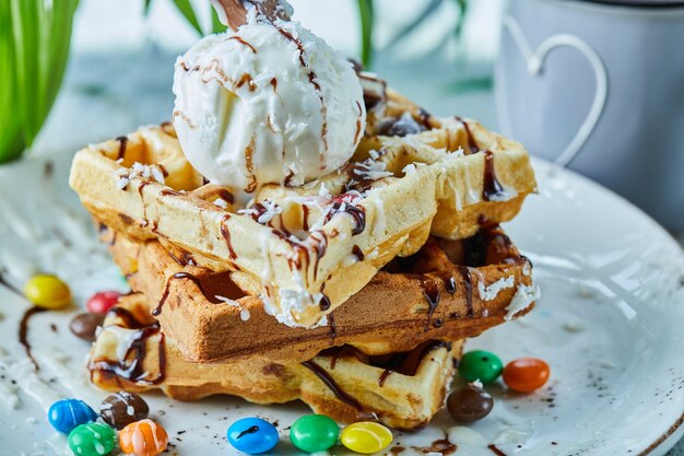 Waffles with ice-cream, chocolate, chocolate balls on the white plate with tea