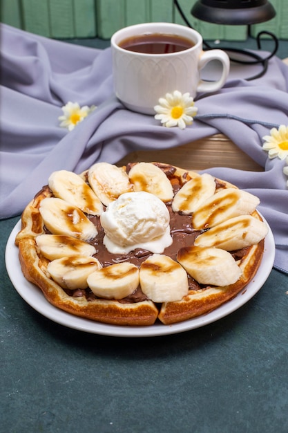 Free Photo waffles with sliced banana, caramel sauce and whipping cream with a cup of tea