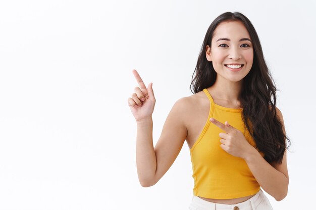 Waist-up attractive young asian female student travelling abroad during education program, see the world, look fascinated and happy, pointing upper left corner and gaze camera carefree