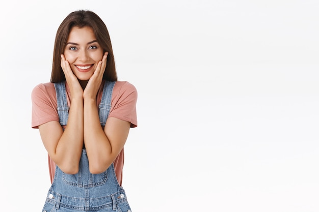 Waist-up portait feminine, cute and happy smiling woman touching pure clean skin and grinning delighted as got rid of blemishes and acne, feeling relived and beautiful, standing white background