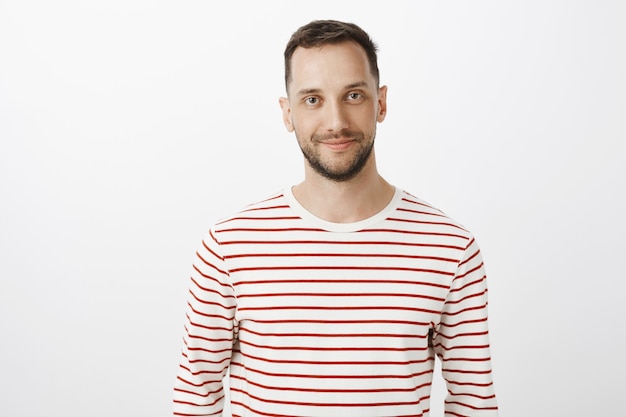 Free photo waist-up portrait of happy calm guy with beard in striped pullover smiling broadly