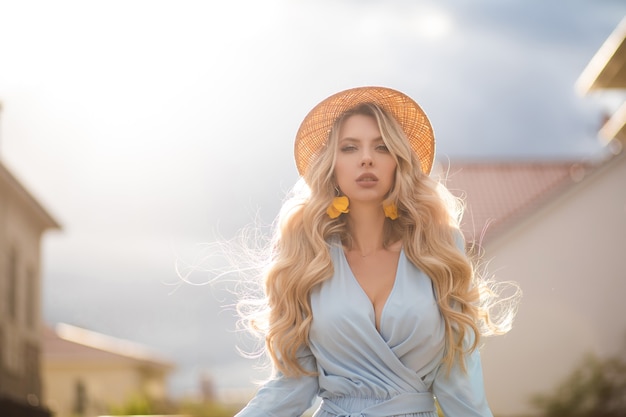 Free photo waist up of pretty young woman wearing summer dress and straw hat while walking on city street. beauty and fashion concept