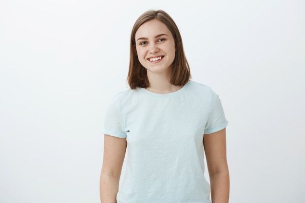 Free Photo waist-up shot of ambitious happy and cute female brunette in trendy t-shirt smiling joyfully being delighted and pleased while receiving congratulations for winning award over white wall