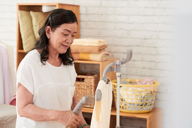 Waist up shot of Asian woman steaming her silk blouse 