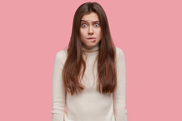 Waist up shot of frustrated worried woman bites lower lip, looks with bewilderment, worries about something