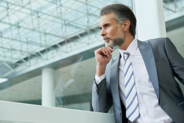 Waist up shot of handsome middle-aged man wearing suit and tie and pondering over new ideas 