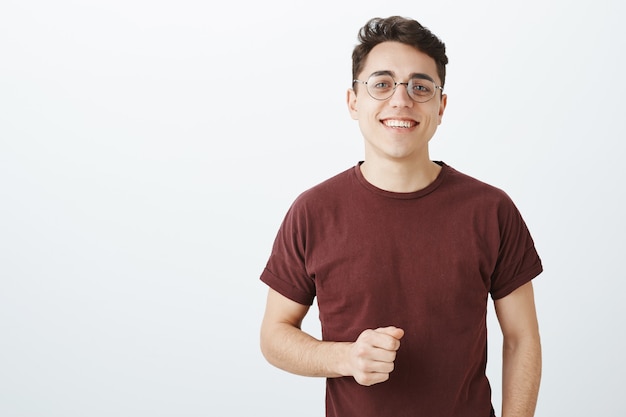 Free photo waist-up shot of happy carefree european male student in trendy round glasses and red t-shirt